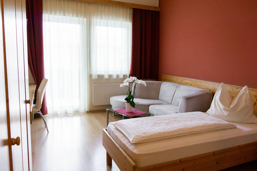 Zimmer mit Doppelbett und Sitzgelegenheit vor roter Wand